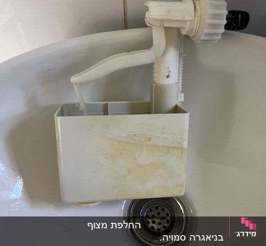 חלק פלסטיק לבן של מנגנון אסלה מונח בכיור